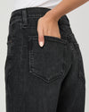 Close-up of a person wearing dark charcoal gray denim jeans, showing the back pocket and hand in the pocket.