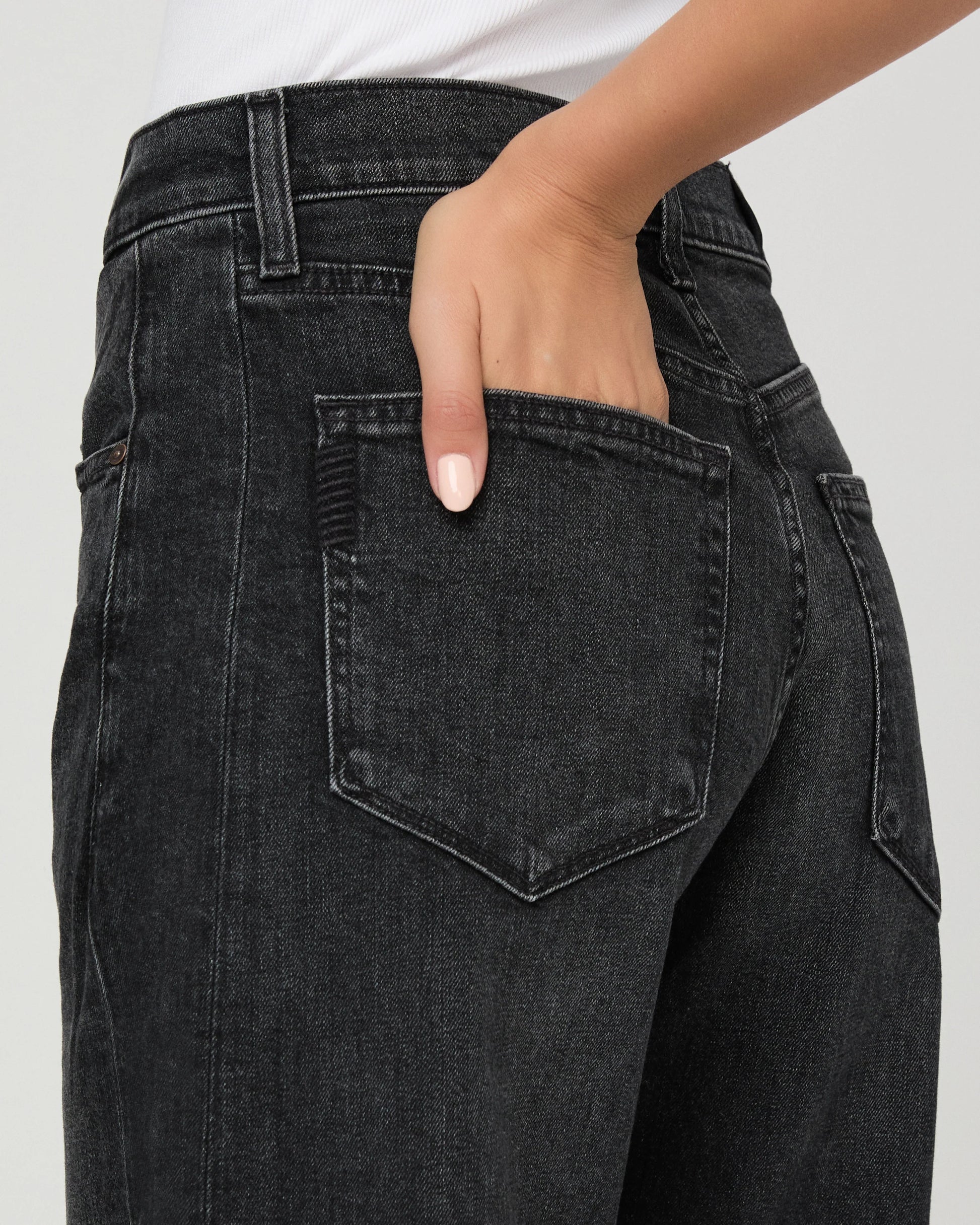 Close-up of a person wearing dark charcoal gray denim jeans, showing the back pocket and hand in the pocket.