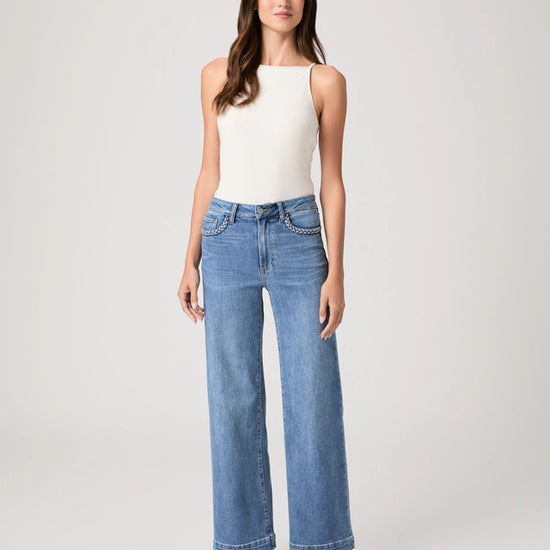 Woman wearing blue jeans and a white top on a plain background