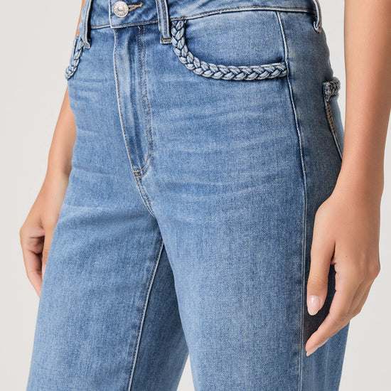 Close-up of blue jeans with a braided detail on a plain background