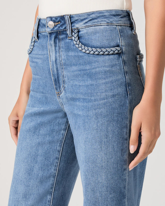 Close-up of blue jeans with a braided detail on a plain background