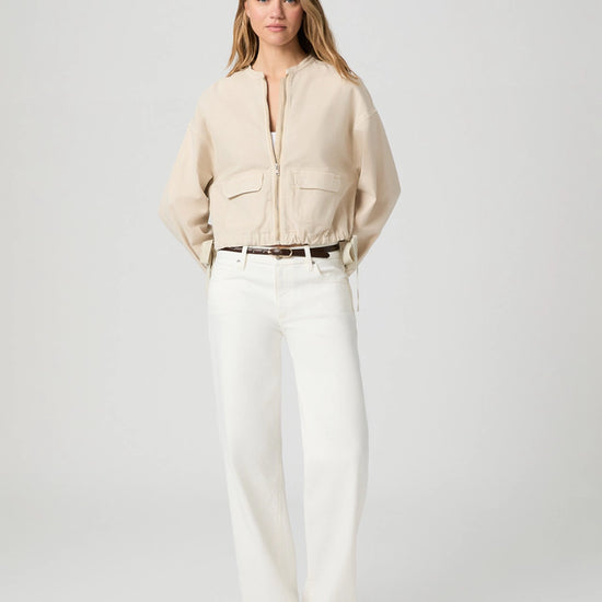 Woman wearing a beige blouse and white pants on a plain background from Paige