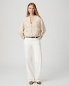 Woman wearing a beige blouse and white pants on a plain background from Paige