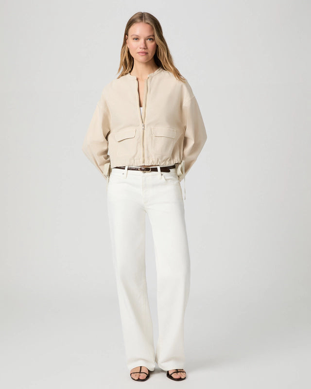 Woman wearing a beige blouse and white pants on a plain background from Paige