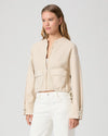 Woman wearing a beige jacket and white pants against a light gray background