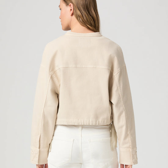 Rear view of model wearing a beige jacket and white pants on a light gray background from Paige