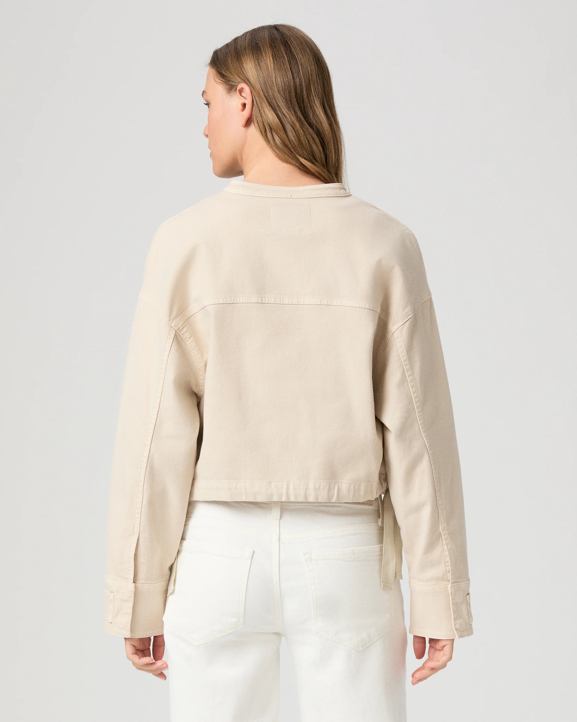 Rear view of model wearing a beige jacket and white pants on a light gray background from Paige