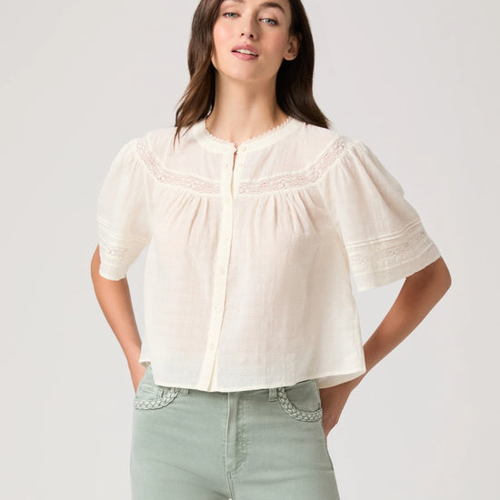 Woman wearing a white blouse by Paige and light green pants on a plain background