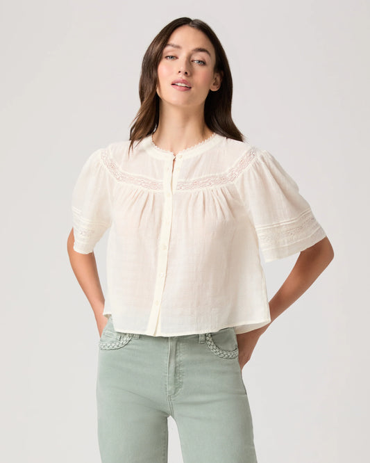 Woman wearing a white blouse by Paige and light green pants on a plain background
