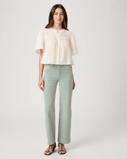 Woman wearing a white blouse by Paige and light green pants on a plain background, showing full outfit 