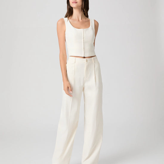 Woman wearing a white sleeveless top and wide-leg pants on a plain background