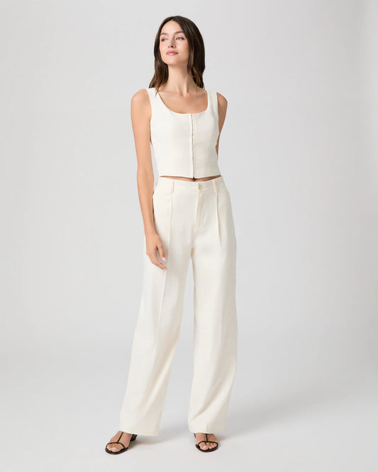 Woman wearing a white sleeveless top and wide-leg pants on a plain background