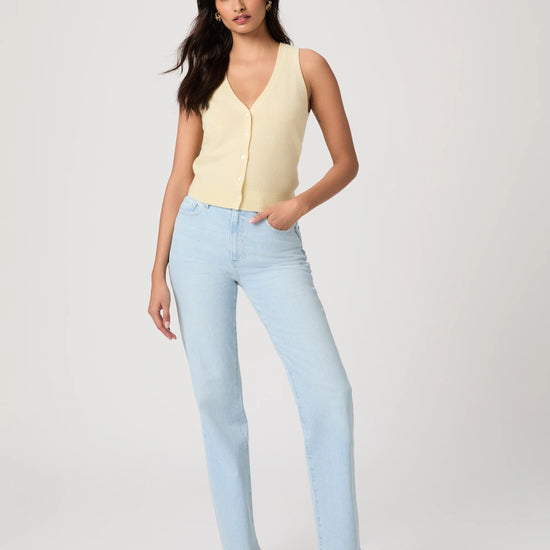 Woman wearing a light yellow sleeveless Paige top and light blue jeans on a plain background, showing full outfit
