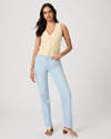 Woman wearing a light yellow sleeveless Paige top and light blue jeans on a plain background, showing full outfit
