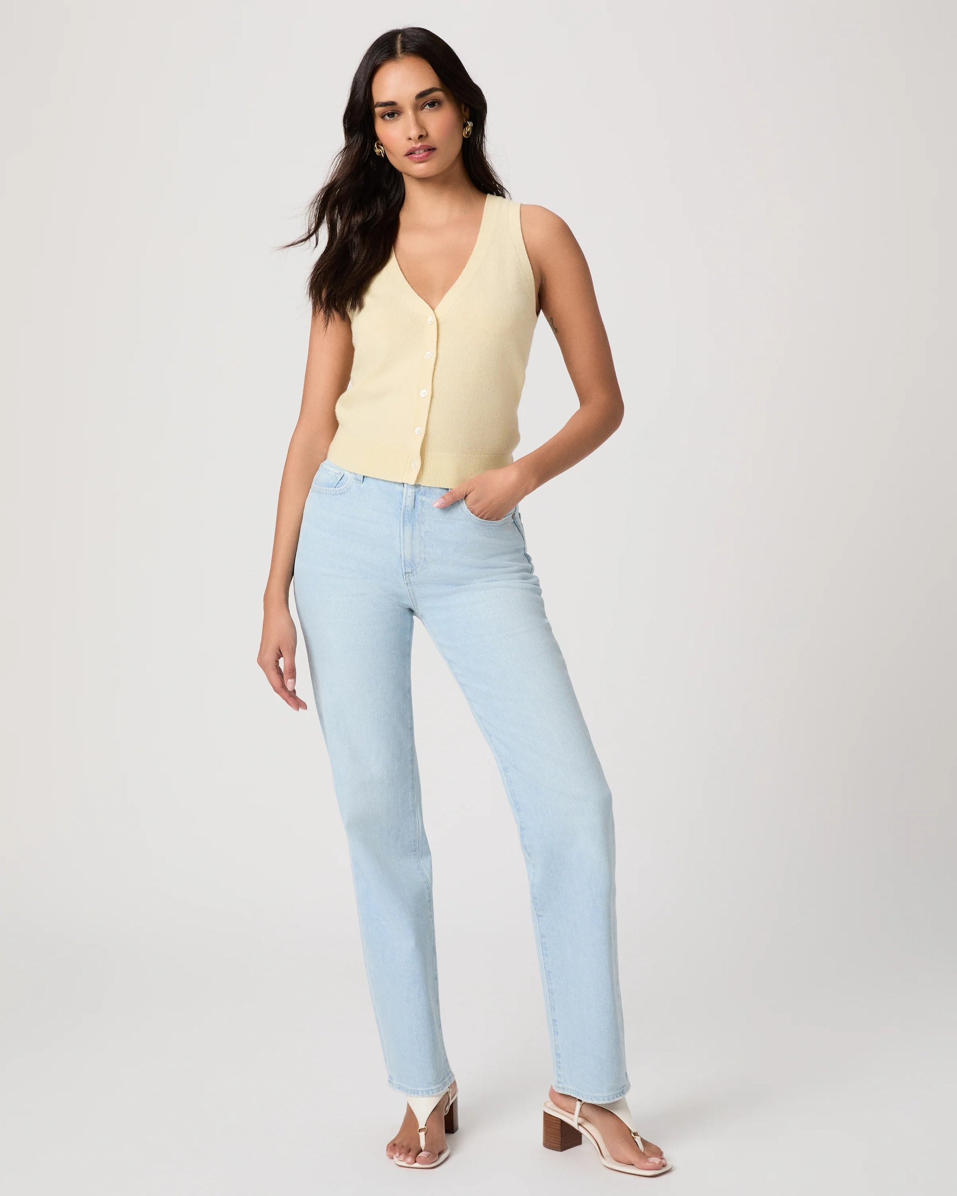 Woman wearing a light yellow sleeveless Paige top and light blue jeans on a plain background, showing full outfit

