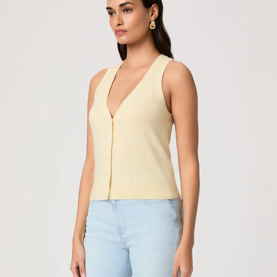 Woman wearing a light yellow sleeveless Paige top and light blue jeans on a plain background side view