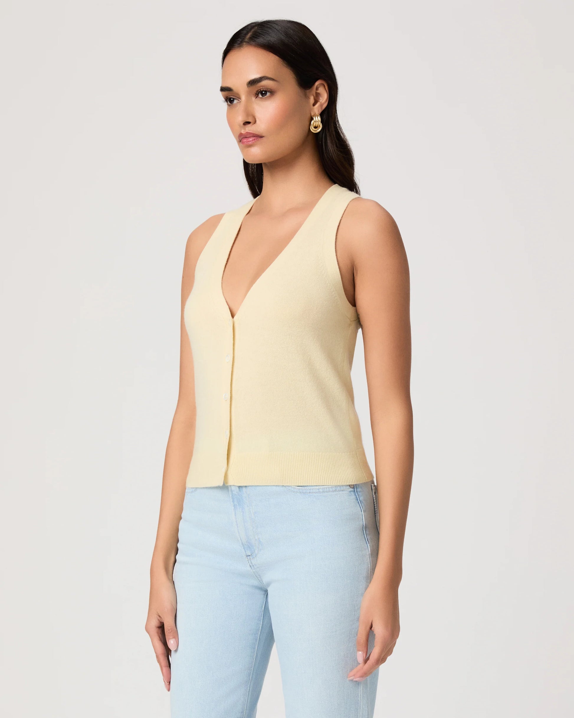 Woman wearing a light yellow sleeveless Paige top and light blue jeans on a plain background side view