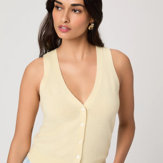 Woman wearing a light yellow sleeveless Paige top and light blue jeans on a plain background close up