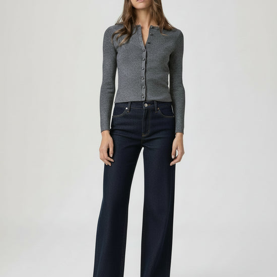 Woman wearing a gray cardigan and dark denim wide leg jeans on a white background