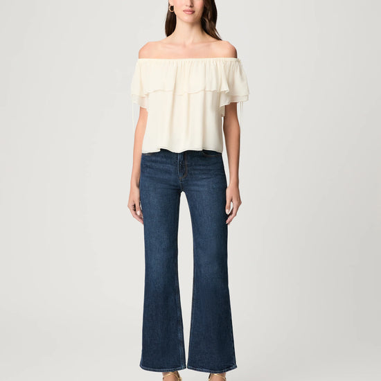 Woman wearing a white off-shoulder top and dark blue jeans on a light gray background