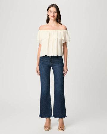 Woman wearing a white off-shoulder top and dark blue jeans on a light gray background