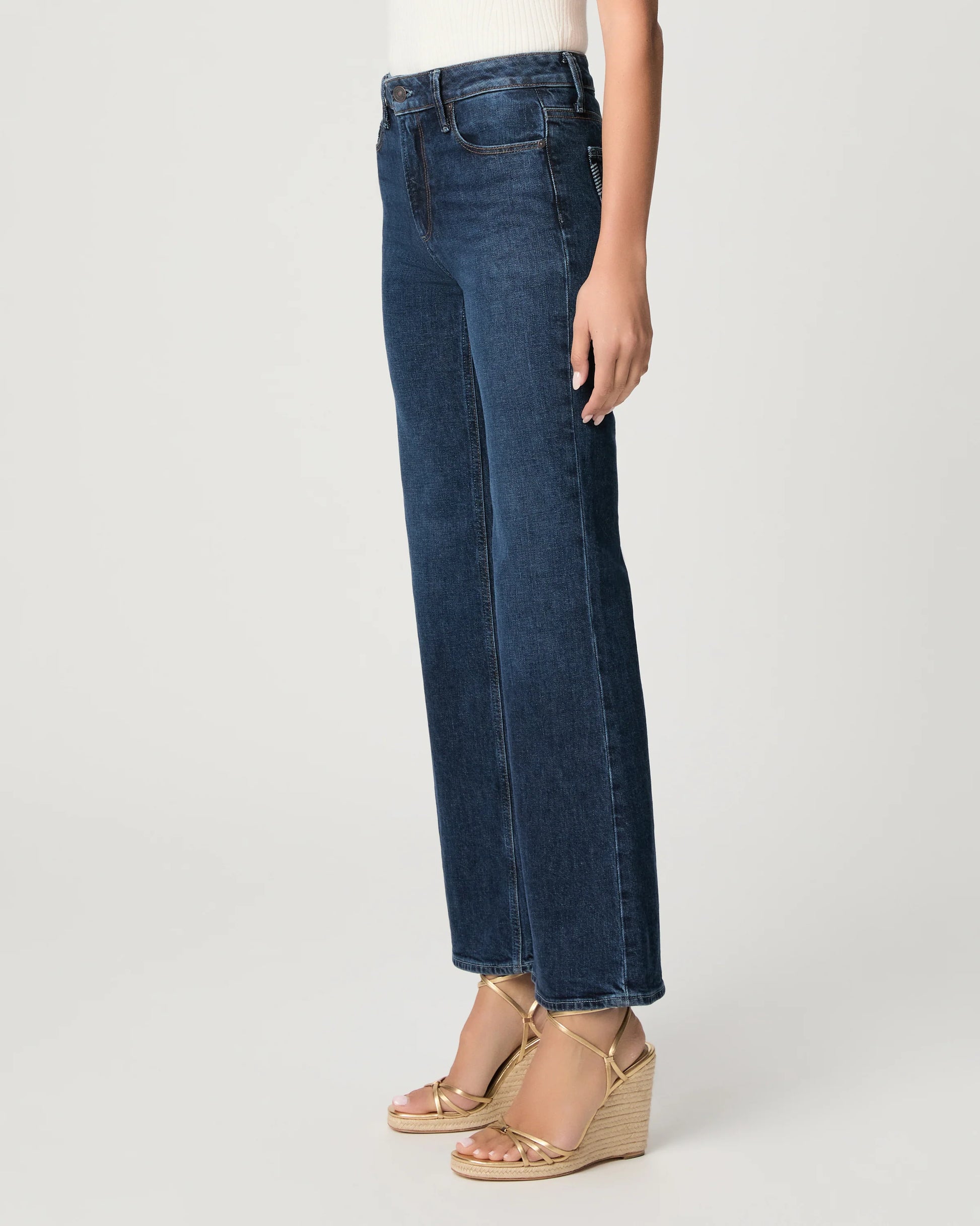 Person wearing blue jeans and gold sandals on a white background