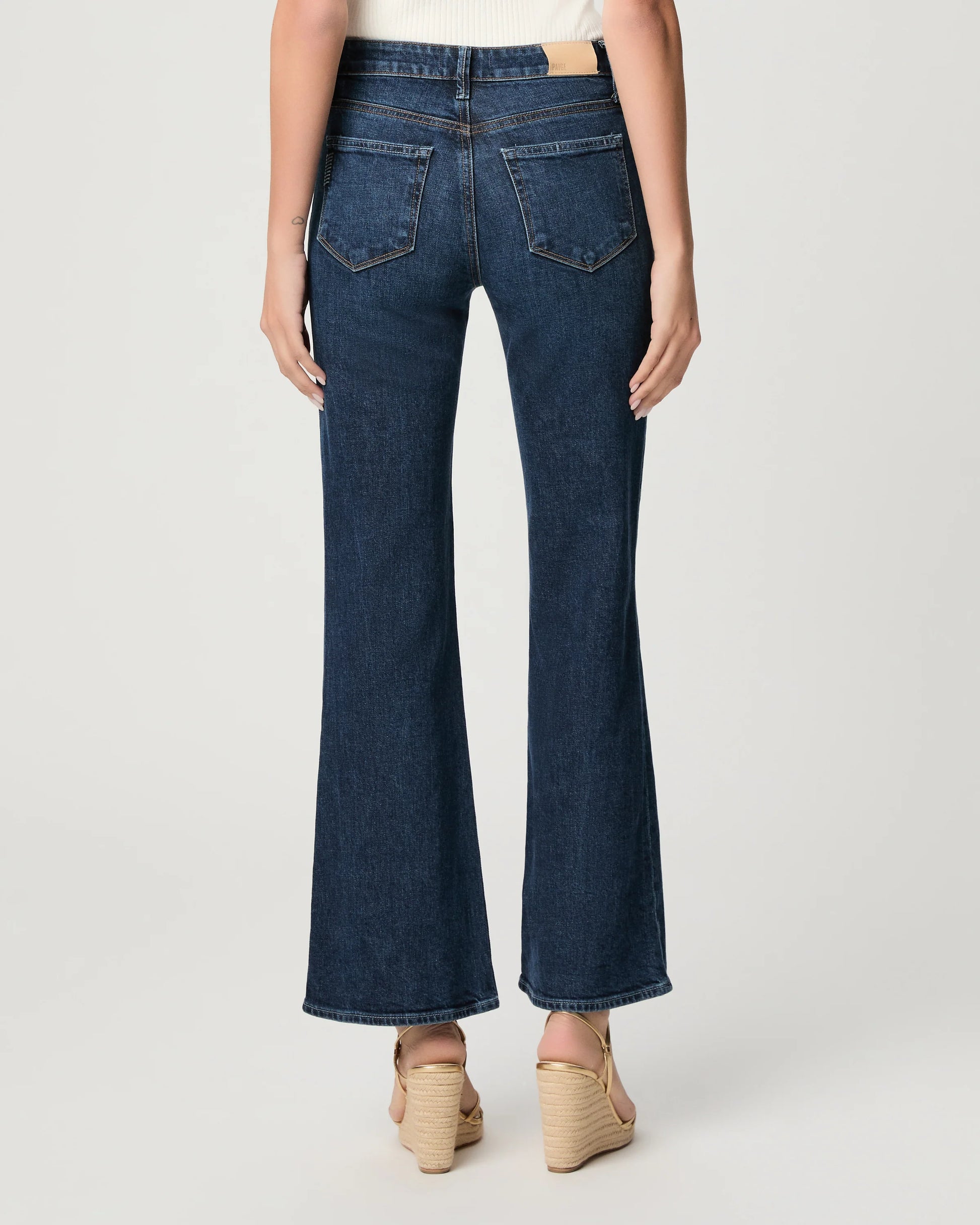 Person wearing dark blue flared jeans on a white background
