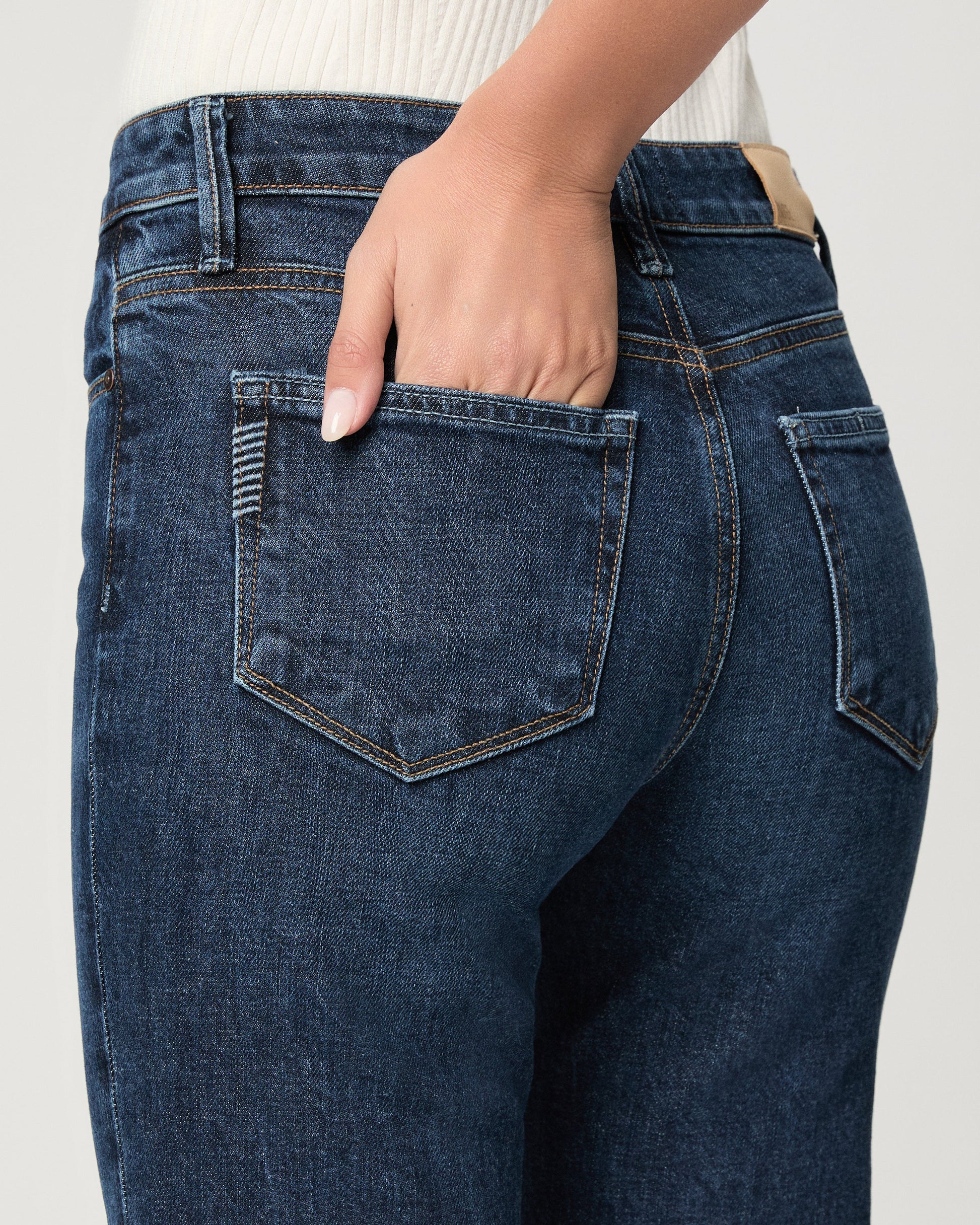 Close-up of blue jeans with a hand in the pocket on a light gray background