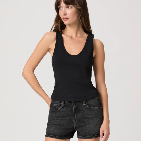 Woman wearing a black tank top and black denim shorts on a light gray background