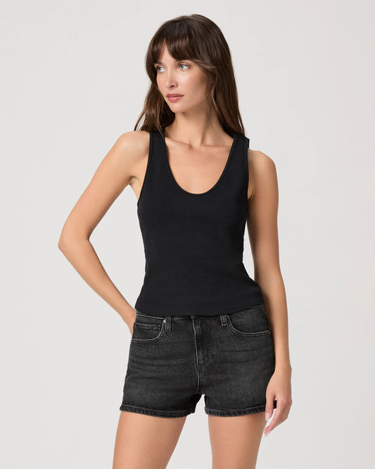 Woman wearing a black tank top and black denim shorts on a light gray background