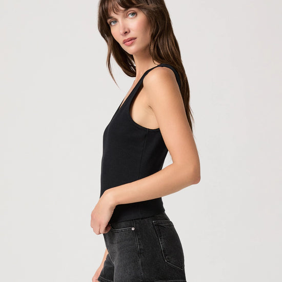 Woman wearing a black tank top and black denim shorts on a light gray background