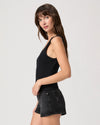 Woman wearing a black tank top and black denim shorts on a light gray background