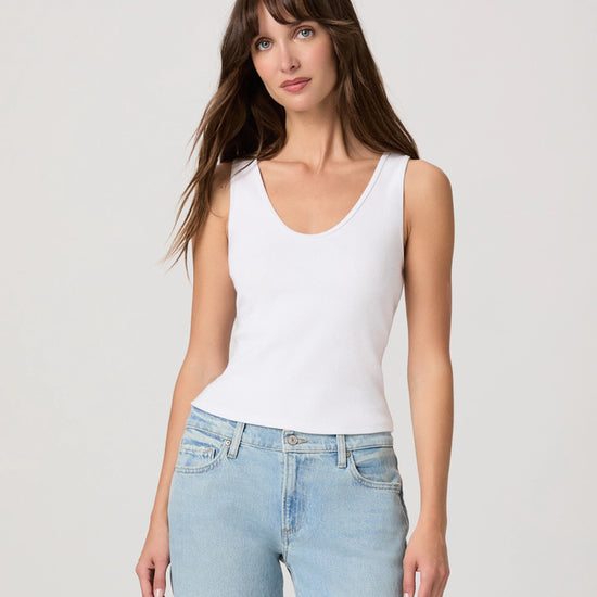 Woman wearing a white tank top and light blue jeans against a plain background