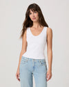 Woman wearing a white tank top and light blue jeans against a plain background
