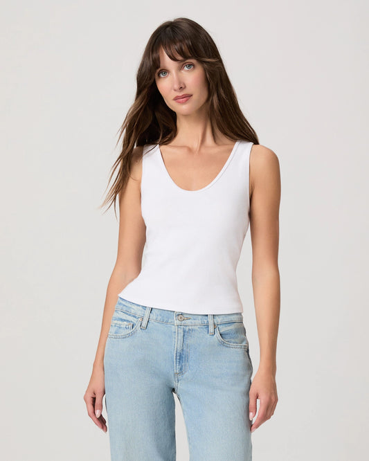 Woman wearing a white tank top and light blue jeans against a plain background