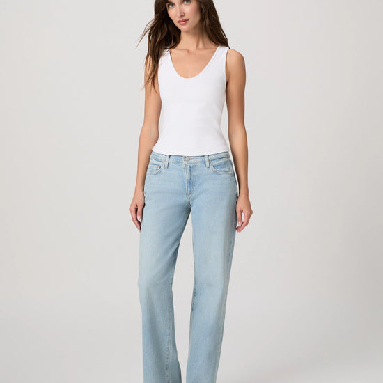 Woman wearing light blue jeans and a white tank top on a plain background
