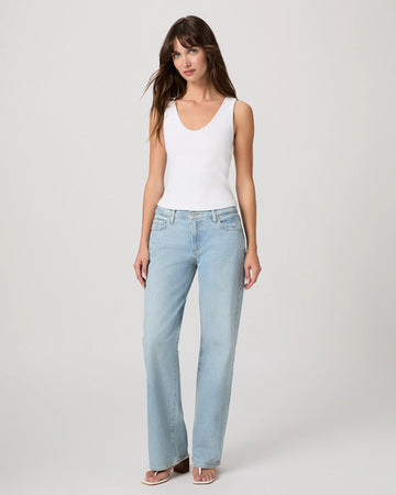 Woman wearing light blue jeans and a white tank top on a plain background