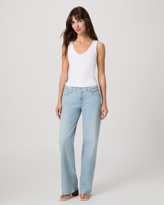 Woman wearing light blue jeans and a white tank top on a plain background