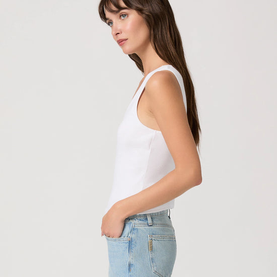 Woman wearing a white tank top and light blue jeans against a plain background