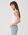 Woman wearing a white tank top and light blue jeans against a plain background