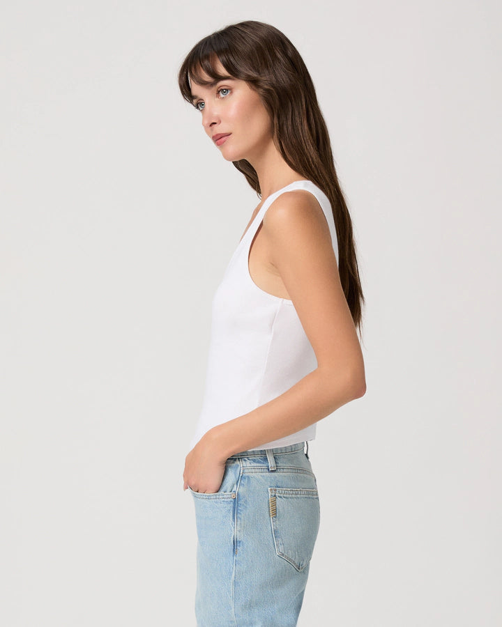 Woman wearing a white tank top and light blue jeans against a plain background