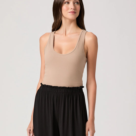 Woman wearing a beige tank top and black pants on a light gray background