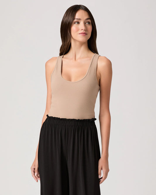 Woman wearing a beige tank top and black pants on a light gray background
