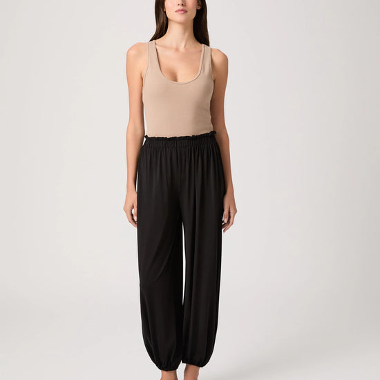 Woman wearing a beige tank top and black wide-leg pants on a white background