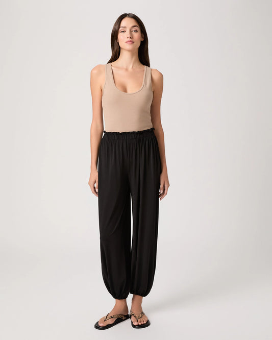 Woman wearing a beige tank top and black wide-leg pants on a white background