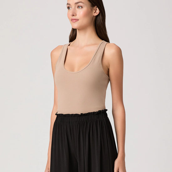 Woman wearing a beige tank top and black pants on a light gray background