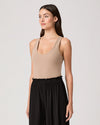 Woman wearing a beige tank top and black pants on a light gray background