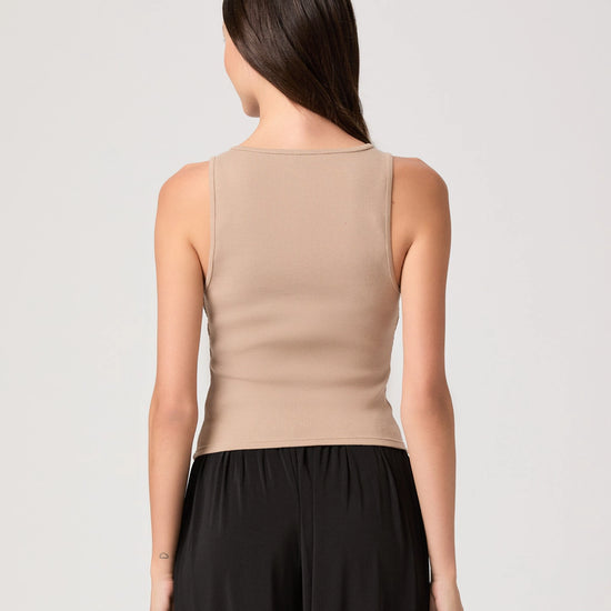 Woman wearing a beige sleeveless top and black pants on a light gray background