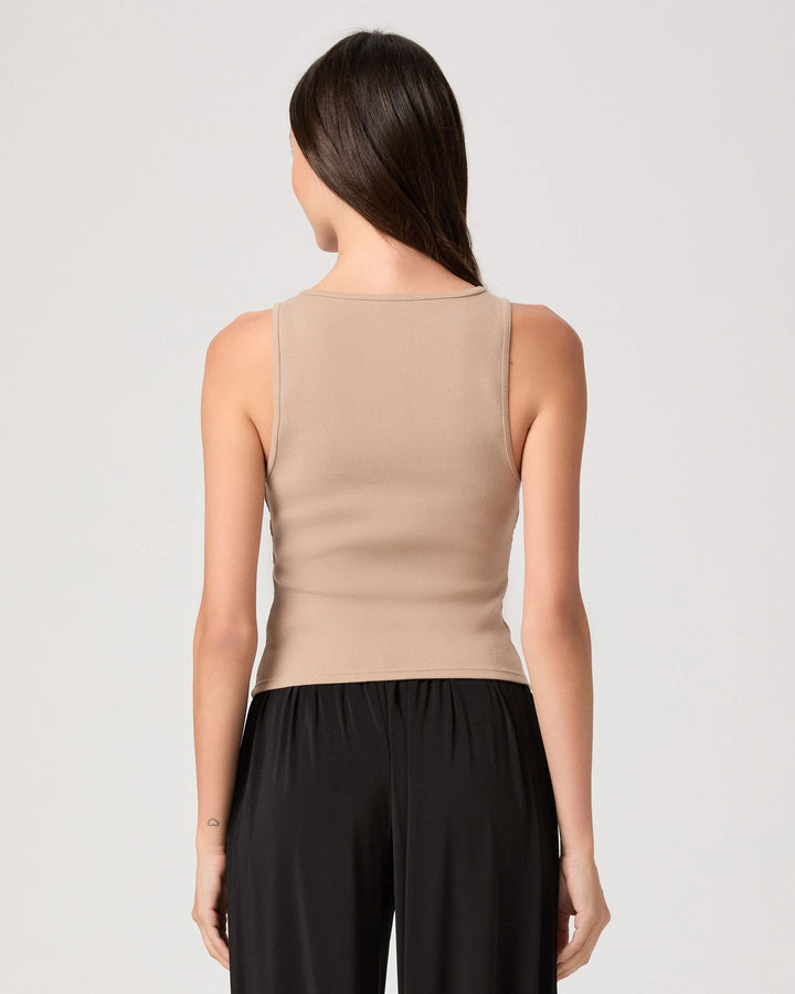 Woman wearing a beige sleeveless top and black pants on a light gray background