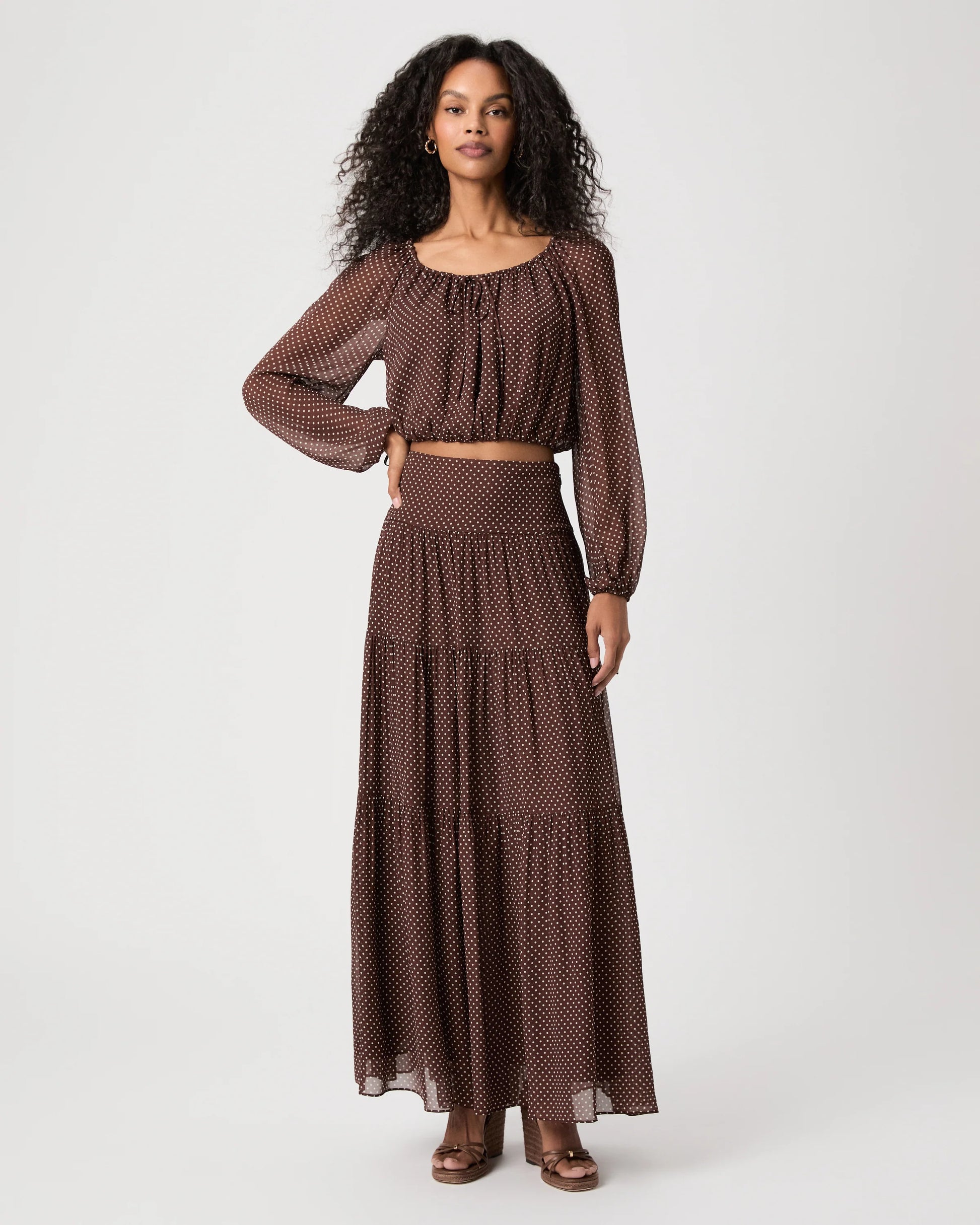 Woman wearing spotty brown and cream blouse and matching skirt on white background